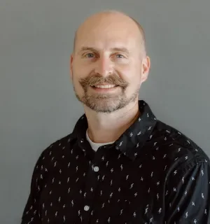 Jared Ponchot wearing a dark button down shirt in front of a gray background.