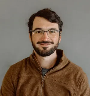 Javier Reartes wearing a brown hoodie in front of a gray background.