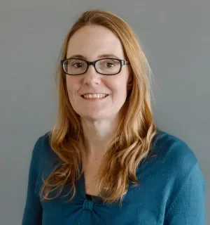 Jen Witkowski wearing a teal top in front of a blue background.