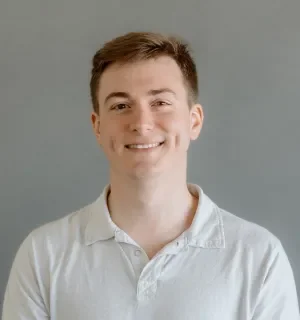 John Kaeser wearing a white polo shirt in front of a gray background.