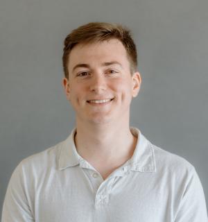 John Kaeser wearing a white polo shirt in front of a gray background.