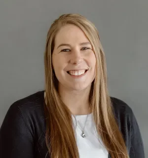 Kayla AhoWalsh wearing a black sweater with white t-shirt in front of a gray background.