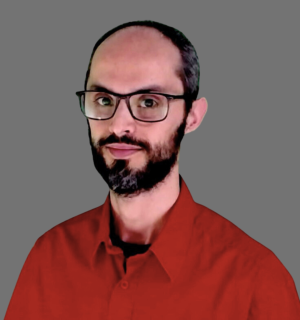 Marcos Cano wearing a red button down shirt and wearing glasses in front of a gray background.