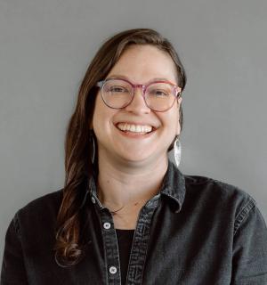 Marissa Epstein wearing glasses and a black button down shirt in front of a gray background.