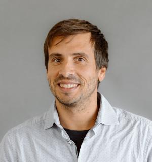 Mateu Aguilo Bosch wearing a white button down shirt with black t-shirt underneath in front of a gray background.
