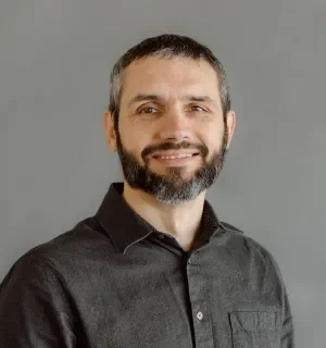 Matt Robison wearing a dark gray button down shirt in front a gray background.