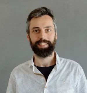 Pablo Lopez Escobes wearing a white button down shirt with a little black dots and a black t-shirt underneath in front of a gray background.