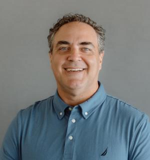 Sean Lange wearing a teal polo shirt in front of a gray background.