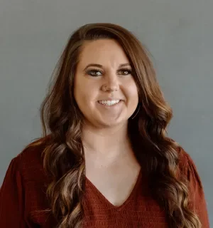 Sydney Barnes in a red v-neck top in front of a gray background.