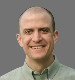 Tim McDorman wearing a light green button down shirt in front of a gray background.