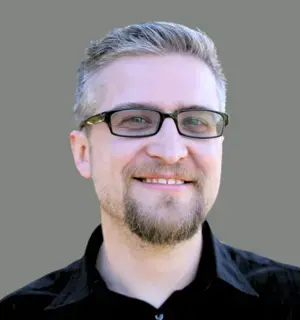 Headshot of Jerad Bitner wearing glasses and black shirt on gray background.
