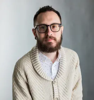 A photograph of Jason Blanda, a 36 year old man with short brown hair, brown eyes, glasses and a tan sweater. 