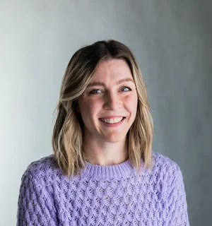 Laura Donelan wearing a purple sweater in front of a gray background.