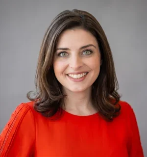 Headshot of Helena McCabe in a red dress. Mid-30's, brown hair, green eyes, caucasian