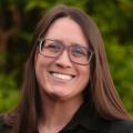 Photo of Lacie Stiewing wearing glasses and a black button-down shirt standing in front of greenery.