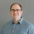 Andy Blum wearing a blue polo shirt in front of gray background.