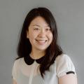 Betty Tran wearing a white blouse with black collar in front of a gray background.