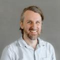 Danny Joris wearing a blue button down shirt in front of a gray background.