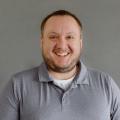 Dave Reid wearing a gray polo shirt in front of a gray background.