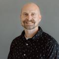 Jared Ponchot wearing a dark button down shirt in front of a gray background.