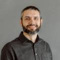 Matt Robison wearing a dark gray button down shirt in front a gray background.