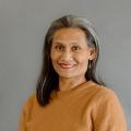 Nikki Flores wearing an orange sweater in front of a gray background.