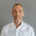 Photo of Seth Brown, white male wearing a white button down oxford shirt in front of a gray background.