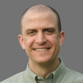 Tim McDorman wearing a light green button down shirt in front of a gray background.