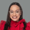Woman with long, dark hair and glasses wearing a red blouse with a bow around her neck.